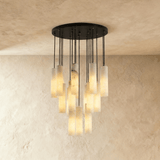 A wide cluster of alabaster cylinders lit, on black cords from a round plate