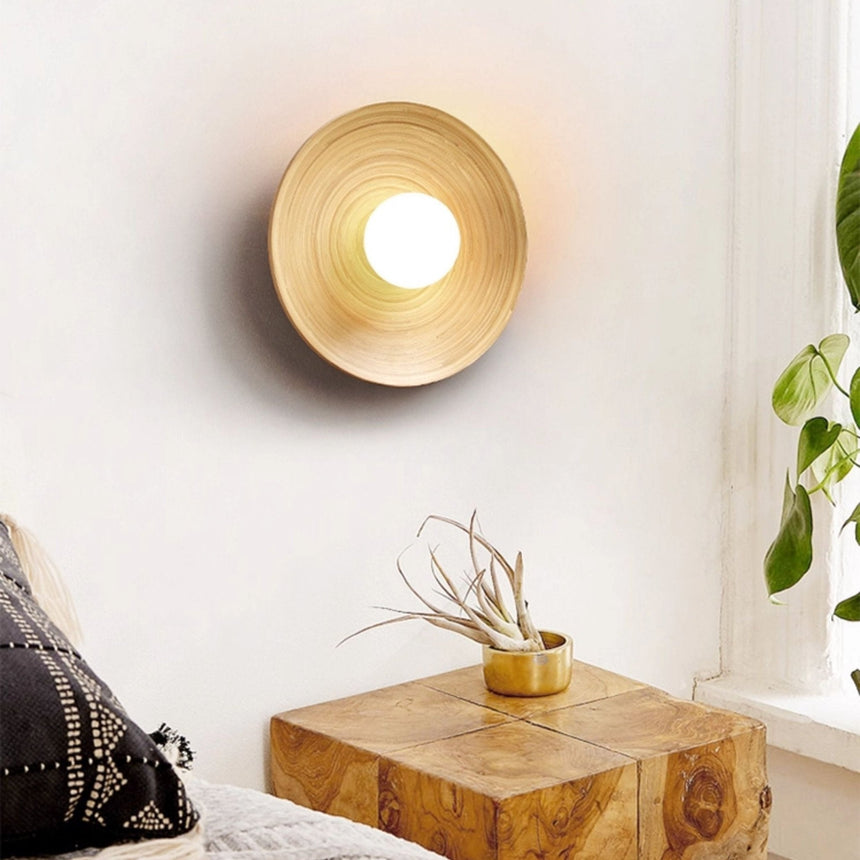 Sconce lit above a bed with a knit cushion and a wood block side table