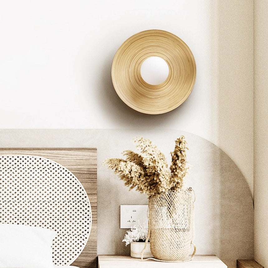Sconce lit beside an arched headboard above dried flowers in a ribbed vase