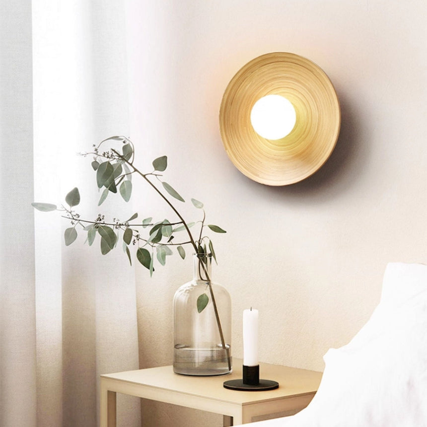 Sconce lit above a nightstand with a candle and a glass vase of leaves