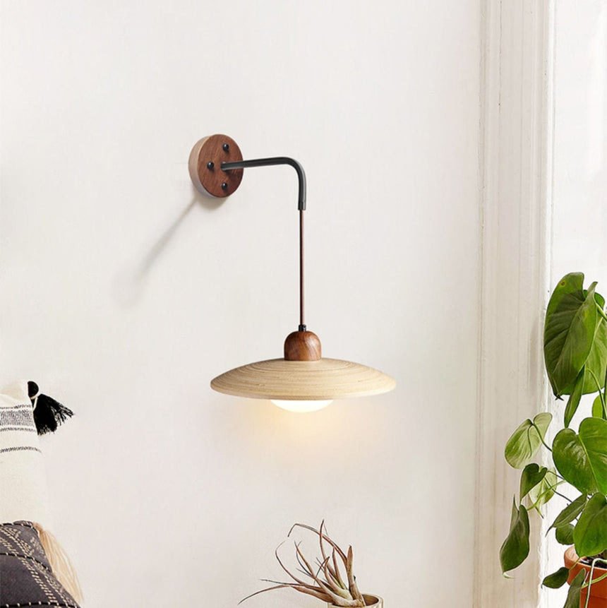 Sconce lit in a room beside a tall plant and a low wood sideboard