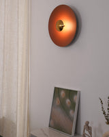 The orange disc lamp above a framed print leaning beside a linen curtain