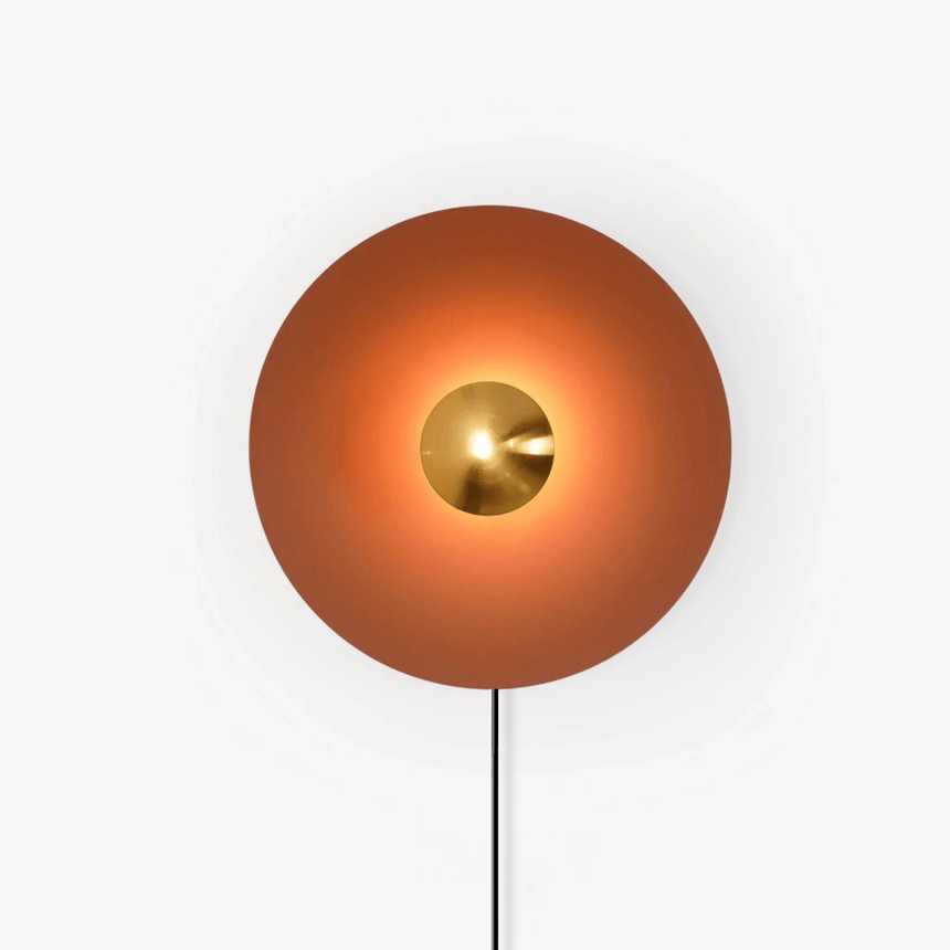 Orange plug in disc wall lamp with a copper tone center and a hanging cord