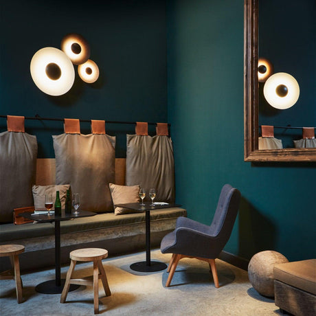 A cluster of disc lamps lit in a teal lounge with an armchair and stools