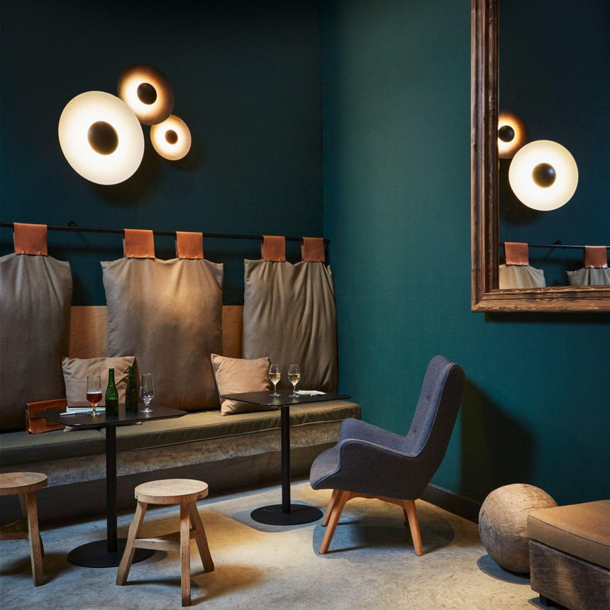 A cluster of disc lamps lit in a teal lounge with an armchair and stools