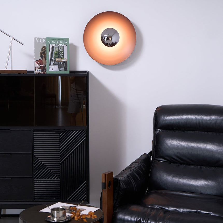 The orange disc light above a black cabinet and a leather armchair