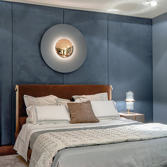 A large disc light glowing on a blue wall above a bed with a leather headboard