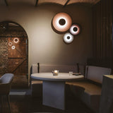 A cluster of three discs lit above a round dining table and a banquette