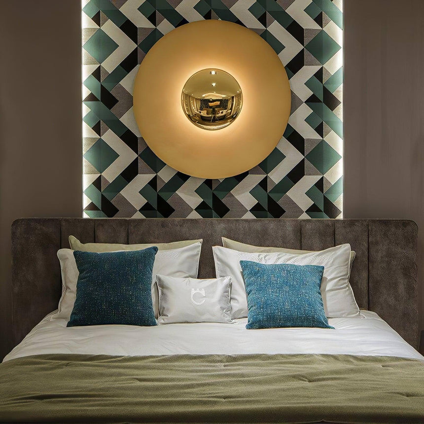 A large disc light glowing above a bed with blue pillows and a patterned wall