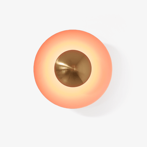 Round orange disc wall light with a copper tone center that glows around its edge
