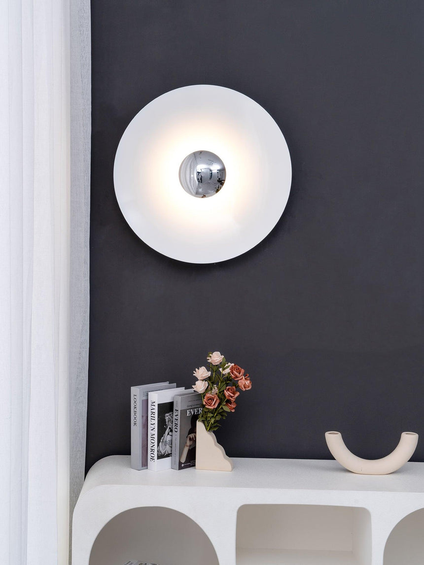 The white disc with a chrome center on a dark wall above a white shelf