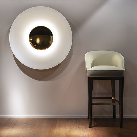 The white disc light lit above a bar stool on a warm gray wall