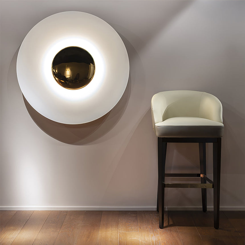 The white disc light lit above a bar stool on a warm gray wall