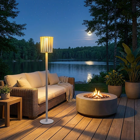 The lamp lit on a deck beside a sofa and a fire bowl facing water