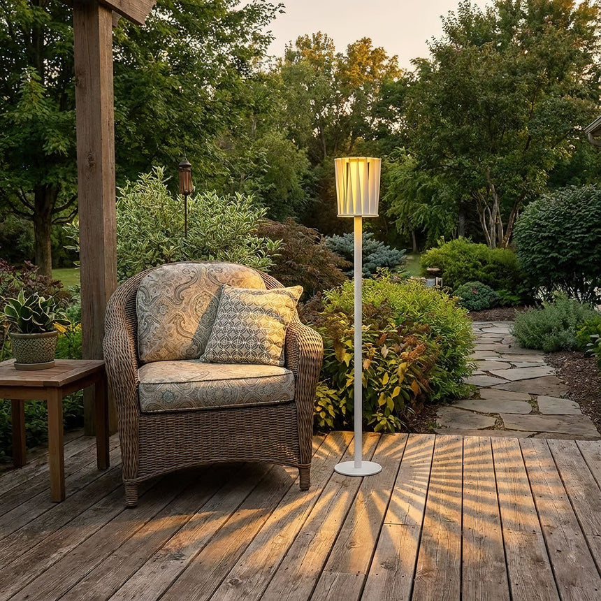 The lamp lit under a timber pergola beside a woven armchair