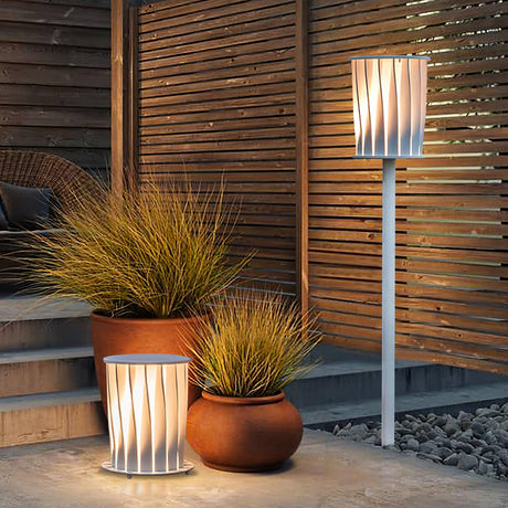 The lamp lit beside terracotta planters and ornamental grasses