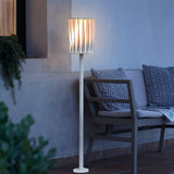 The lamp lit against a pale render wall beside a slatted bench
