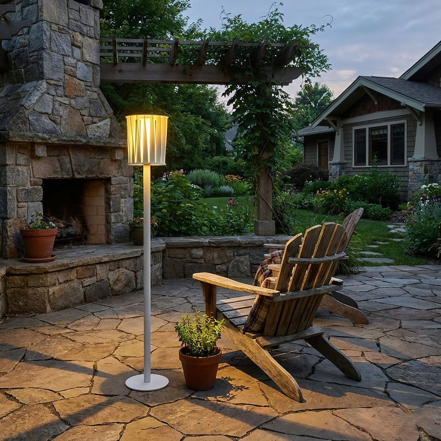 The lamp lit on a stone terrace beside a timber chair and a pot