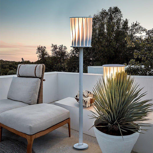The lamp lit on a terrace beside a low sofa and a tall planted pot