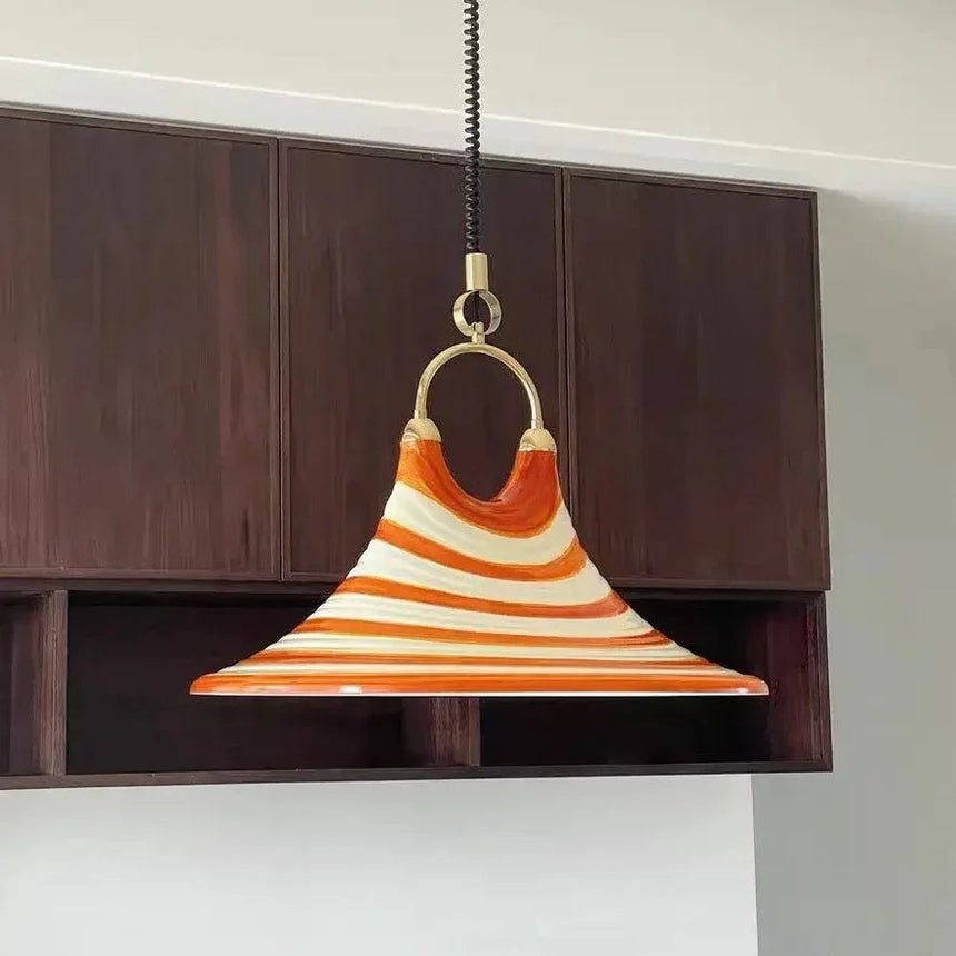 The striped orange glass cone lit above a dark wooden sideboard