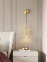 The brass cone above a white nightstand with books beside an upholstered bed