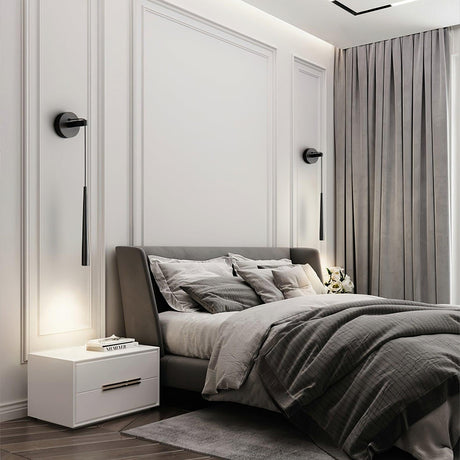 A pair of black cones lit on each side of a bed with gray linens