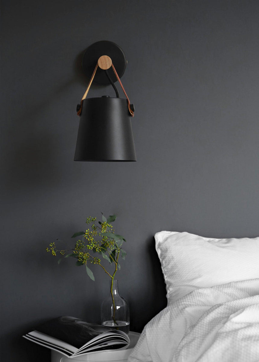 Sconce lit on a dark wall beside a bed with a plant on the nightstand