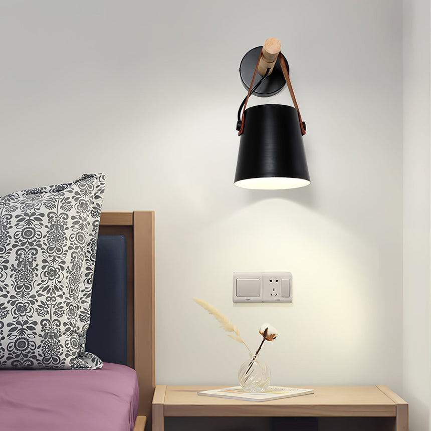 Sconce lit beside a bed above a nightstand holding a small dried stem