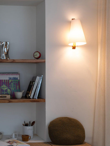 Sconce lit beside built in shelves holding books and a stone bowl