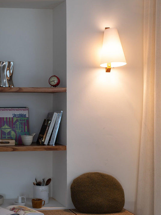 Sconce lit beside built in shelves holding books and a stone bowl