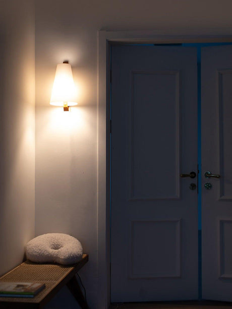 Sconce lit beside a panel door above a low bench with a round cushion