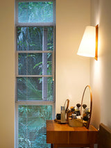 Sconce lit beside a slatted blind above a dressing table with small jars