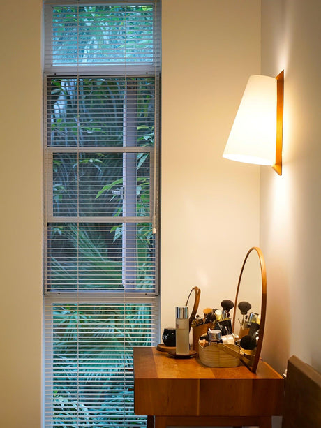 Sconce lit beside a slatted blind above a dressing table with small jars