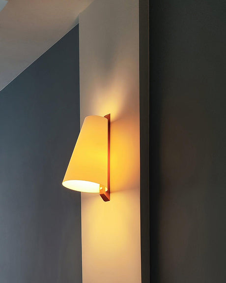 Sconce lit on a deep blue wall, the cone glowing against the flat color