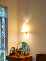 Sconce lit beside a mirror above a wood dressing table and a window