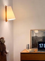 Sconce lit above a wood desk with a framed print, a laptop and a small toy