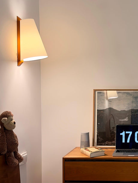 Sconce lit above a wood desk with a framed print, a laptop and a small toy