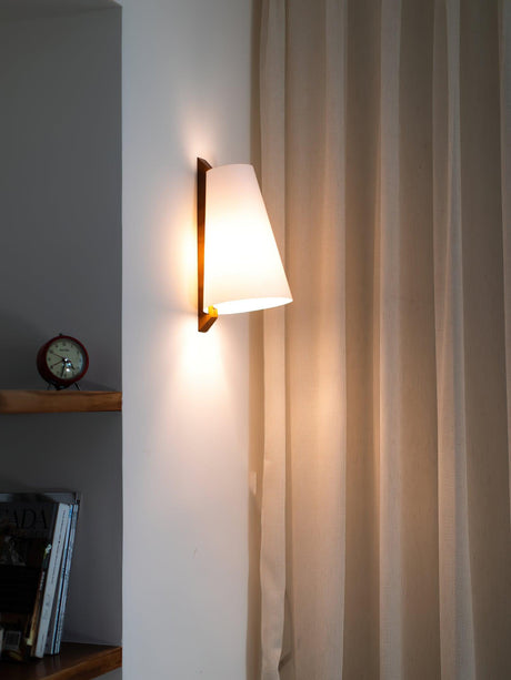 Sconce lit beside a curtain above a shelf with a clock and stacked books