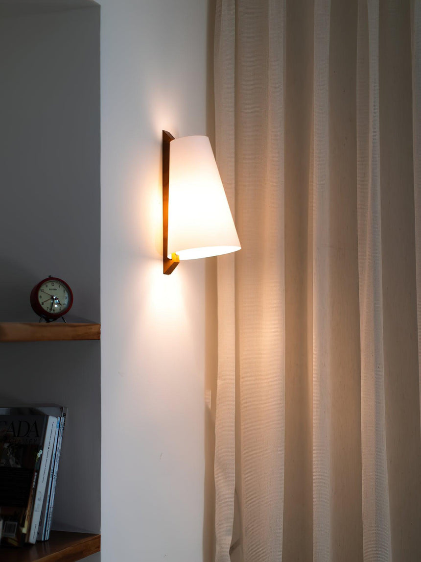 Sconce lit beside a curtain above a shelf with a clock and stacked books