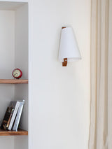 Sconce lit above a narrow shelf holding books and a small round clock