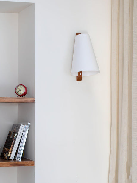 Sconce lit above a narrow shelf holding books and a small round clock