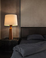Console table lamp in walnut lit on a nightstand beside a bed