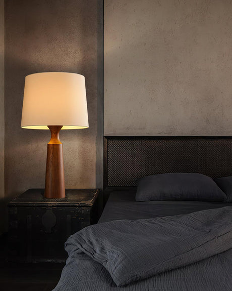 Console table lamp in walnut lit on a nightstand beside a bed