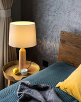 Console table lamp lit on a round side table beside a made bed
