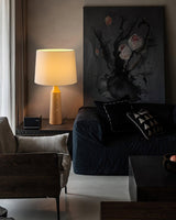 Console table lamp lit beside a dark bed and a framed picture