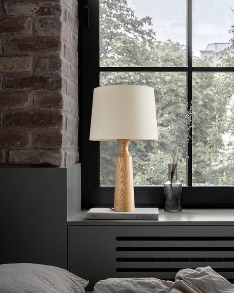 Console table lamp with a white shade lit on a windowsill