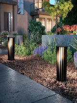 Two lit along a planted border beside a paved terrace at night