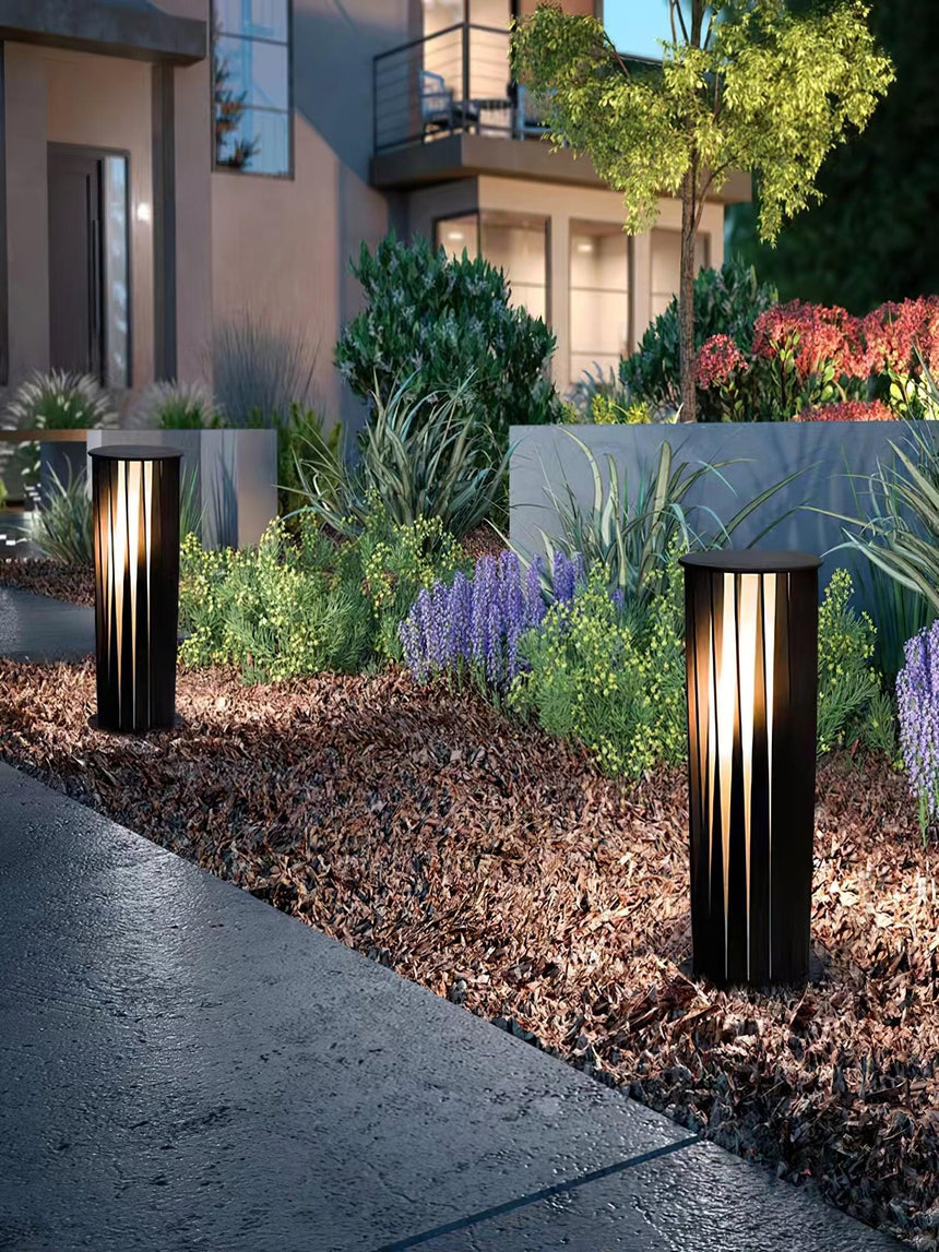 Two lit along a planted border beside a paved terrace at night