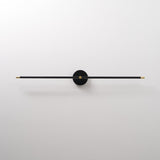 The black rod seen unlit, a thin bar through a round hub on a pale wall