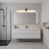 Dark rod lit above a long mirror in a white bathroom beside a glass shower
